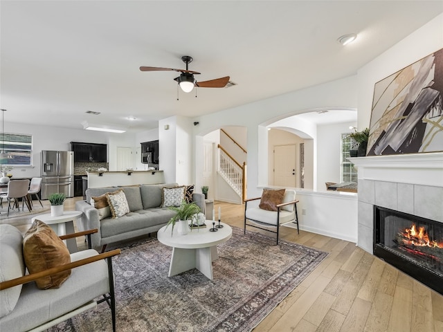 living room with arched walkways, light wood-type flooring, stairway, a ceiling fan, and healthy amount of natural light