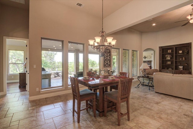 dining space featuring arched walkways, stone tile flooring, a towering ceiling, ceiling fan, and a chandelier