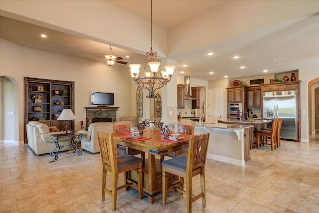 dining room featuring arched walkways, recessed lighting, a chandelier, light stone finish flooring, and a fireplace