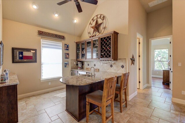 kitchen with a sink, decorative backsplash, stone tile floors, glass insert cabinets, and a breakfast bar area