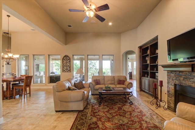 living room with built in shelves, ceiling fan, arched walkways, a high ceiling, and a fireplace