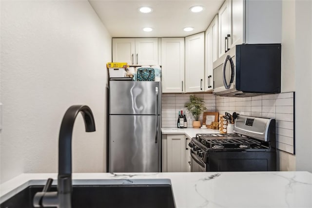 kitchen featuring stainless steel appliances, a sink, decorative backsplash, white cabinetry, and recessed lighting