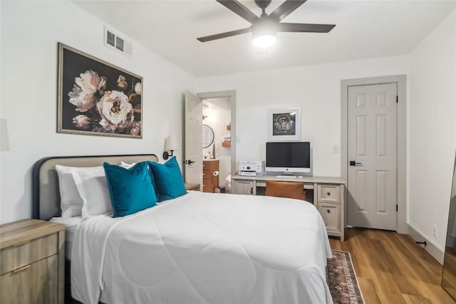 bedroom featuring wood finished floors, a desk, ceiling fan, and ensuite bathroom