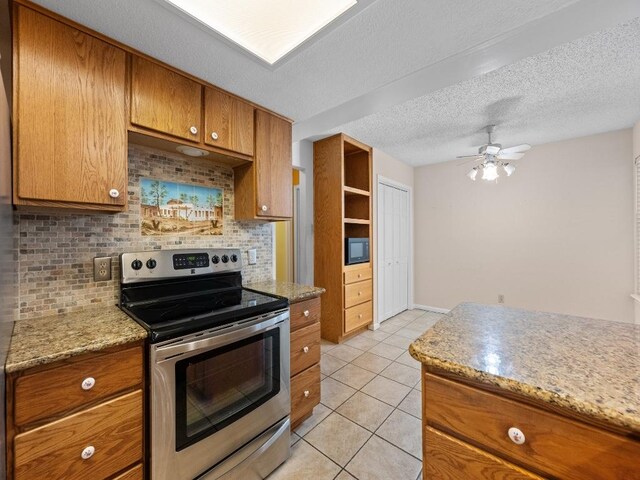 3606 Spotted Horse Trl, Austin, TX 78739 - kitchen featuring stainless steel range with electric cooktop, brown cabinets, tasteful backsplash, light tile patterned flooring, and a ceiling fan