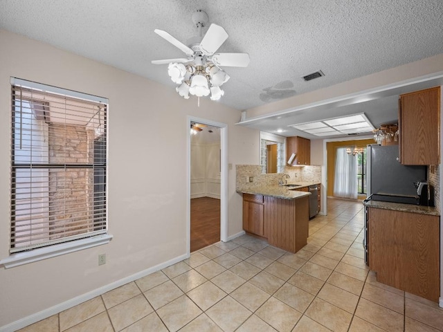 3606 Spotted Horse Trl, Austin, TX 78739 - kitchen with a peninsula, appliances with stainless steel finishes, light tile patterned flooring, brown cabinetry, and a textured ceiling