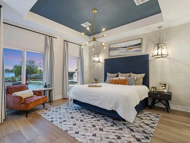 710 Bernese Pass, Austin, TX 78745 - bedroom featuring a tray ceiling, a chandelier, brick wall, and wood finished floors