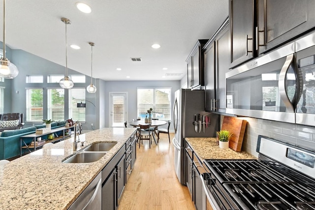 7308 Oberon St, Austin, TX 78741 - kitchen featuring stainless steel appliances, light wood-style flooring, decorative backsplash, light stone countertops, and decorative light fixtures