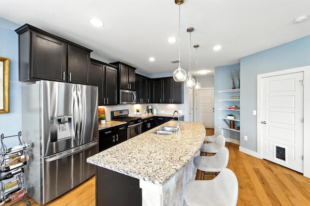 7308 Oberon St, Austin, TX 78741 - kitchen with appliances with stainless steel finishes, a sink, light wood-style floors, light stone counters, and a center island with sink