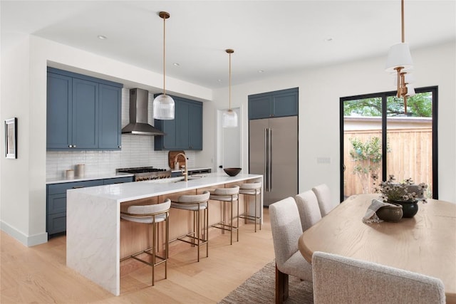 1703 Madison Ave, Austin, TX 78757 - kitchen featuring high end fridge, wall chimney range hood, blue cabinetry, light wood finished floors, and recessed lighting