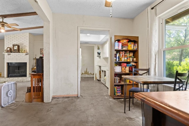 dining space with a ceiling fan, a textured ceiling, concrete floors, and a fireplace