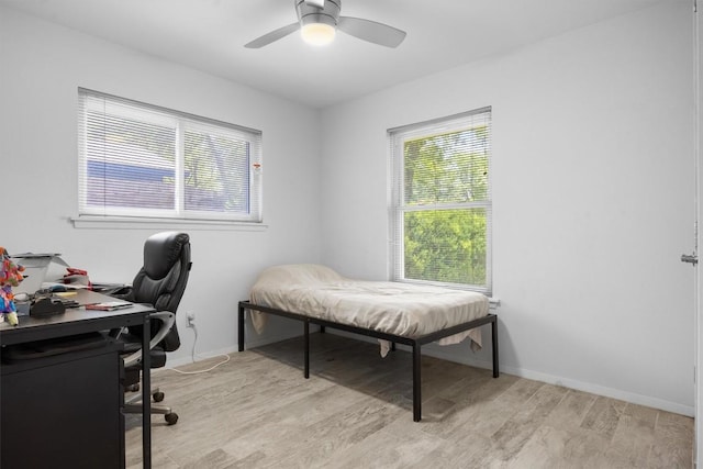 bedroom featuring light wood-style floors, an office area, baseboards, and a ceiling fan