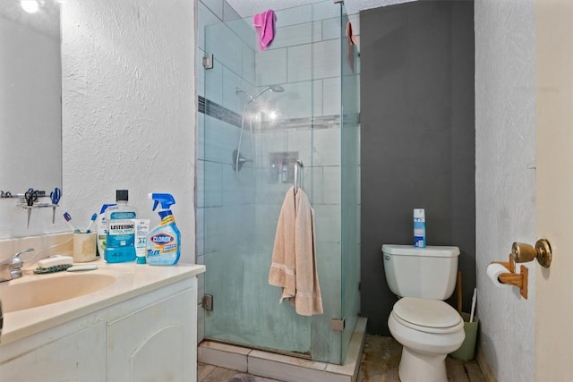 full bath with a stall shower, a textured wall, toilet, and vanity