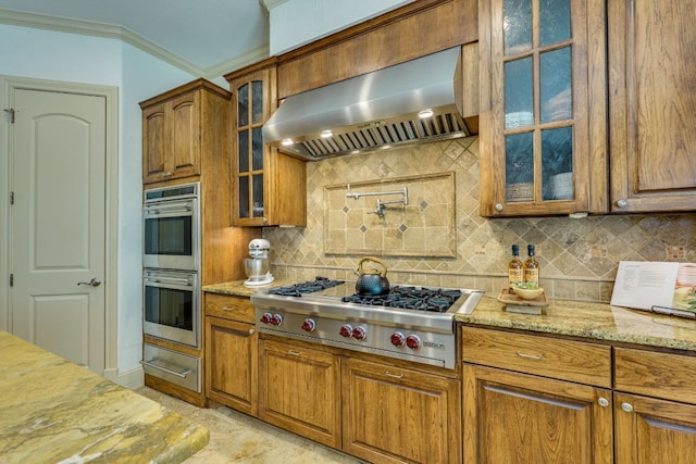 1186 Ranchers Club Ln, Driftwood, TX 78619 - kitchen featuring exhaust hood, appliances with stainless steel finishes, brown cabinetry, light stone countertops, and crown molding
