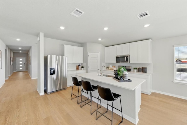kitchen featuring stainless steel appliances, a sink, a breakfast bar area, light countertops, and a center island with sink