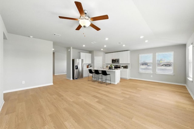 unfurnished living room with a sink, light wood-style floors, a ceiling fan, baseboards, and lofted ceiling