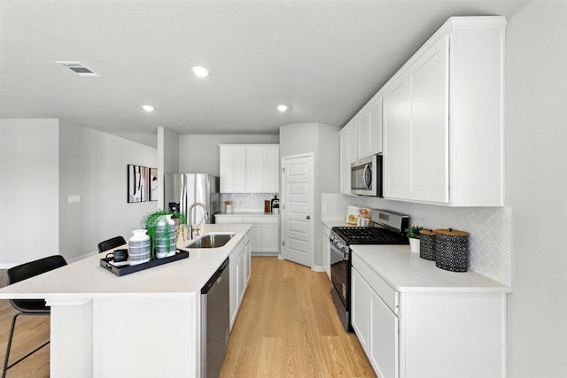 kitchen featuring stainless steel appliances, a kitchen breakfast bar, a sink, light wood finished floors, and decorative backsplash