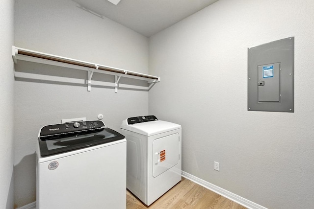 laundry area with electric panel, washing machine and clothes dryer, light wood-style floors, and baseboards