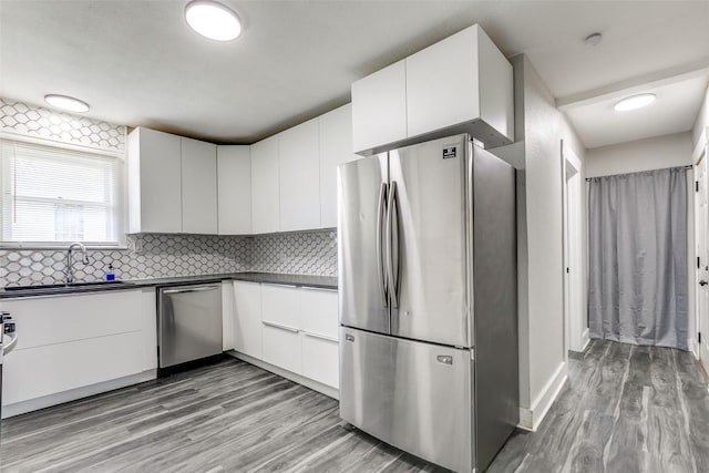 kitchen with appliances with stainless steel finishes, dark countertops, white cabinets, and light wood-type flooring