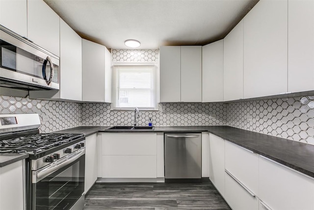 kitchen with appliances with stainless steel finishes, a sink, dark countertops, and white cabinets