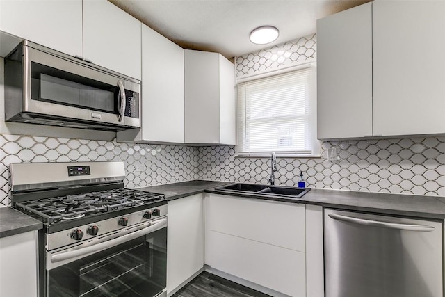 kitchen with stainless steel appliances, a sink, dark countertops, and white cabinets