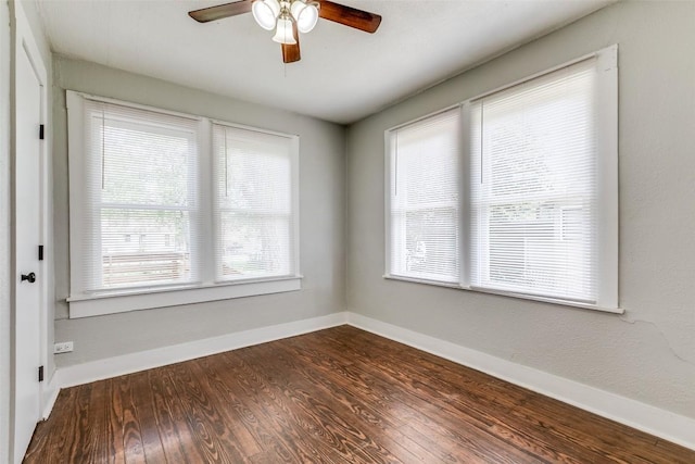 unfurnished room featuring plenty of natural light, a ceiling fan, dark wood finished floors, and baseboards