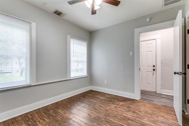 empty room with plenty of natural light, dark wood finished floors, and a ceiling fan