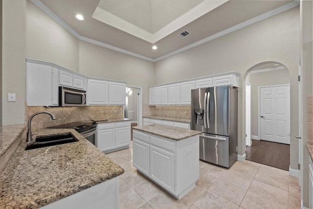 kitchen with stainless steel appliances, a towering ceiling, a sink, arched walkways, and light stone counters