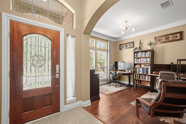 tiled foyer featuring arched walkways, crown molding, a chandelier, and baseboards