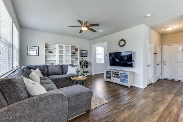 living room with healthy amount of natural light, ceiling fan, and dark wood-type flooring