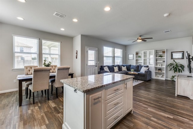 kitchen with ceiling fan, dark wood finished floors, recessed lighting, light stone countertops, and a kitchen island