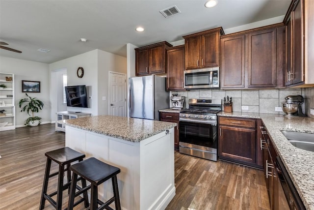 kitchen featuring stainless steel appliances, a center island, dark wood-style floors, light stone countertops, and recessed lighting