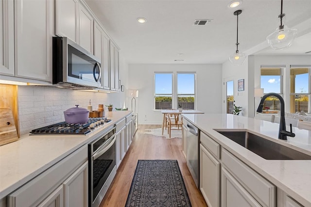 424 Turnbuckle Bnd, Leander, TX 78641 - kitchen featuring stainless steel appliances, a sink, tasteful backsplash, light wood-style flooring, and pendant lighting