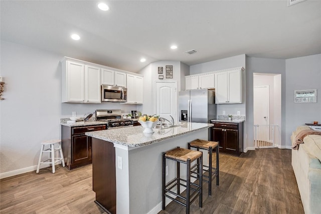 kitchen featuring appliances with stainless steel finishes, baseboards, a kitchen breakfast bar, wood finished floors, and recessed lighting