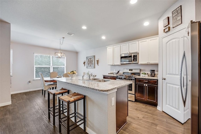 kitchen featuring appliances with stainless steel finishes, a kitchen breakfast bar, a sink, light wood-style floors, and recessed lighting