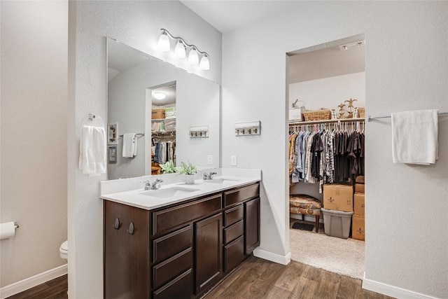 bathroom featuring wood finished floors, a spacious closet, double vanity, toilet, and baseboards