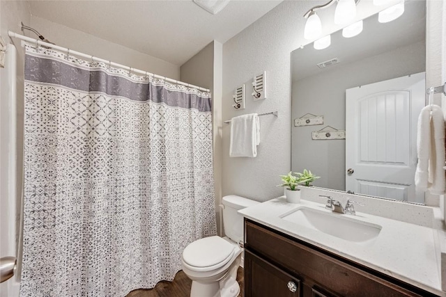 full bathroom with toilet, vanity, and a textured wall