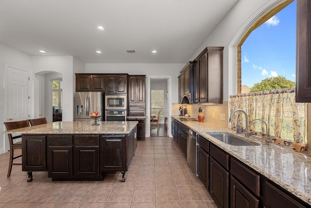 kitchen with appliances with stainless steel finishes, a sink, arched walkways, a kitchen island, and recessed lighting