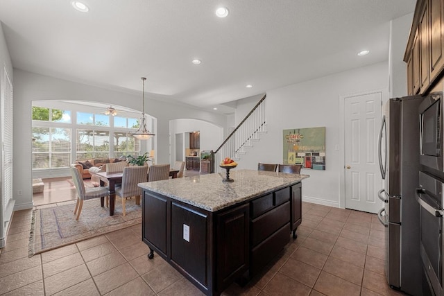 kitchen featuring arched walkways, dark tile patterned floors, a kitchen island, light stone counters, and recessed lighting