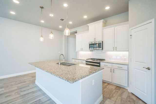 kitchen with stainless steel appliances, a sink, a center island with sink, light wood-type flooring, and light stone countertops