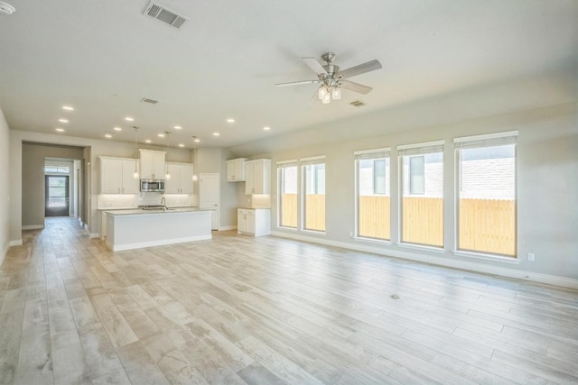 unfurnished living room featuring ceiling fan, a sink, baseboards, light wood-type flooring, and recessed lighting