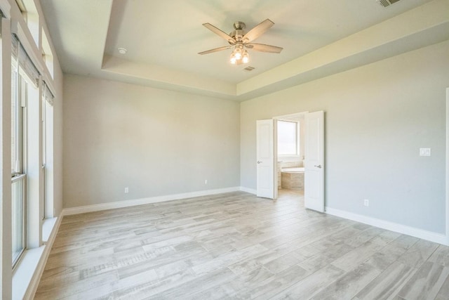 unfurnished room featuring a ceiling fan, a tray ceiling, baseboards, and light wood-type flooring