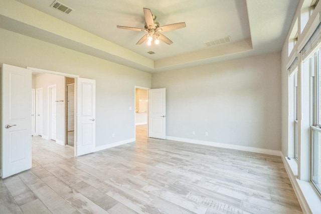 unfurnished bedroom with light wood-style flooring, a tray ceiling, baseboards, and a ceiling fan