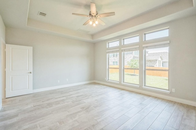 unfurnished room featuring a raised ceiling, a ceiling fan, baseboards, and light wood-type flooring