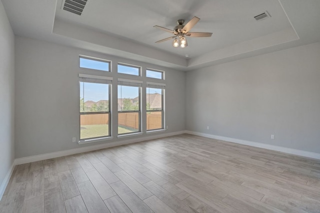 spare room featuring a tray ceiling, ceiling fan, light wood-style flooring, and baseboards