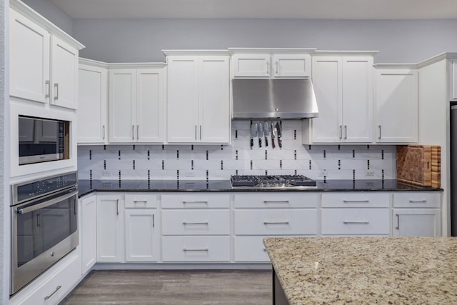 3405 Eagle Ridge Ln, Pflugerville, TX 78660 - kitchen with stainless steel appliances, under cabinet range hood, white cabinetry, dark stone countertops, and light wood finished floors