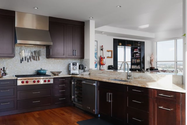 kitchen featuring wall chimney range hood, a sink, stainless steel gas cooktop, tasteful backsplash, and light stone countertops