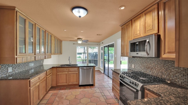 kitchen featuring appliances with stainless steel finishes, a peninsula, a sink, backsplash, and a ceiling fan