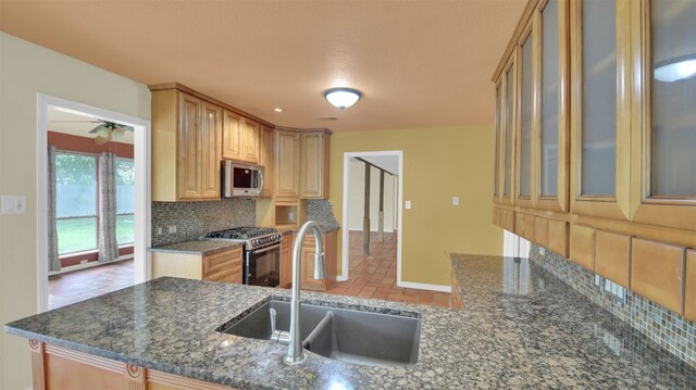 kitchen with stainless steel appliances, a sink, tasteful backsplash, glass insert cabinets, and dark stone counters