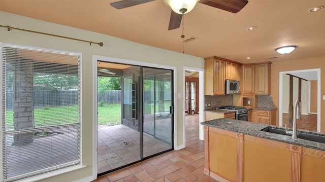 kitchen featuring appliances with stainless steel finishes, a sink, tasteful backsplash, ceiling fan, and brick floors