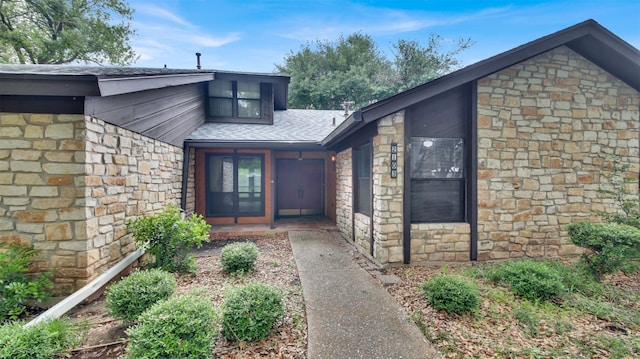 view of exterior entry with stone siding and a shingled roof